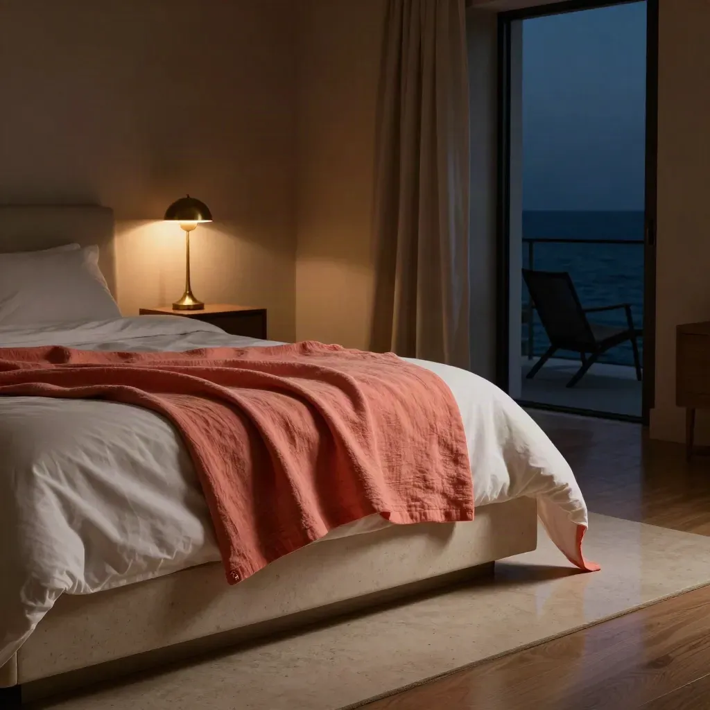 Suite notturna con plaid corallo, lampada accesa e finestra aperta sul mare.
